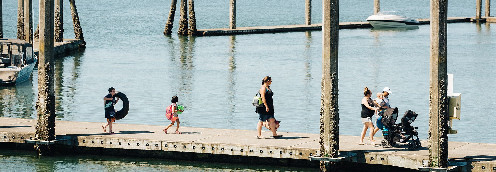 A group of parents and young children walk along the pier carrying their water toys.